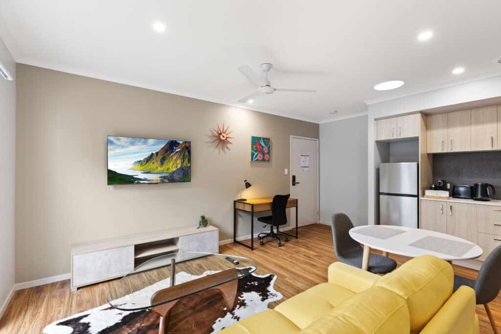 Modern Brisbane rooming house living room with open-plan kitchen and comfortable furnishings.